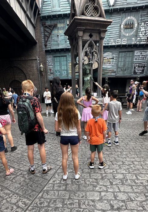 The kids gather with wands raised around a fountain statue, hoping to trigger its magic.