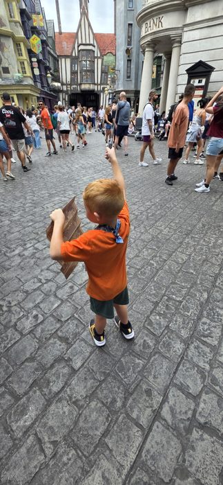 One of the kids darts through Diagon Alley with wand raised and map in hand.