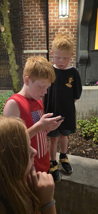 Two of the kids huddle over a phone outside the bakery at night while another looks on.
