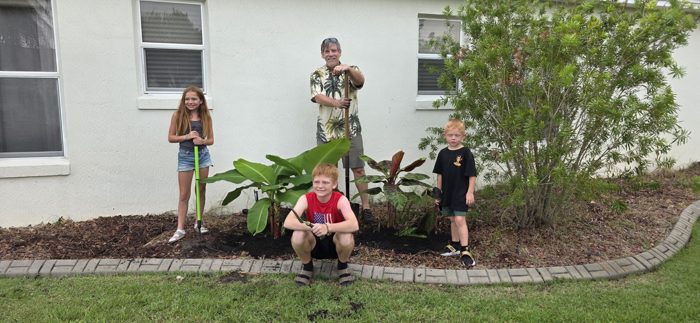 The family gathers once more by the new landscaping, tools resting against their shoulders.