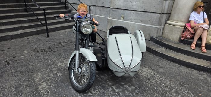 One of the kids playing motorcycle driver on a vintage sidecar prop outside the shops.