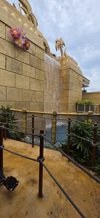 A carved stone waterfall and painted tropical flowers line the queue path at the park.