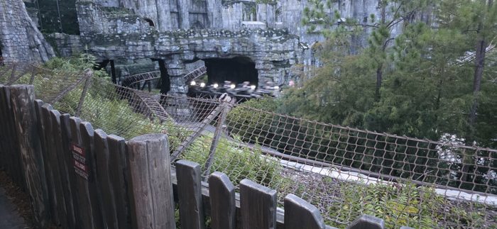 A coaster train slips out from beneath the ancient ruins as evening light fades.