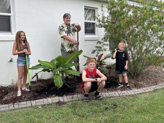 The kids line up with their garden tools beside freshly planted banana trees at a family stop in Florida.