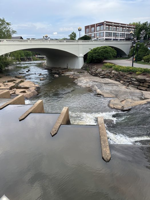 A flat road bridge spanning the river above the rocky weir.