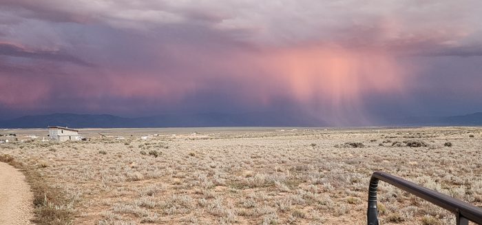 Layered pink and gold storm clouds glow over the distant mountains from camp.