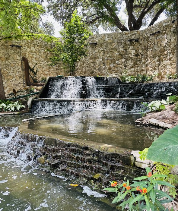 A tiered waterfall feature spilling into the River Walk canal.