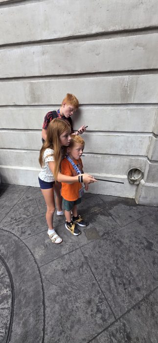 The kids huddle together trying out their new wands against the castle wall.