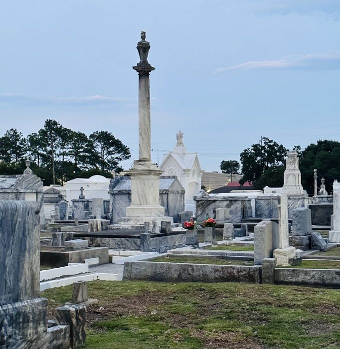A tall monument column rises above a sea of crosses and tombs in the old cemetery.