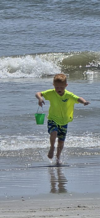 One of the kids dashes through the surf, green bucket swinging, mid-shriek at the cold water.