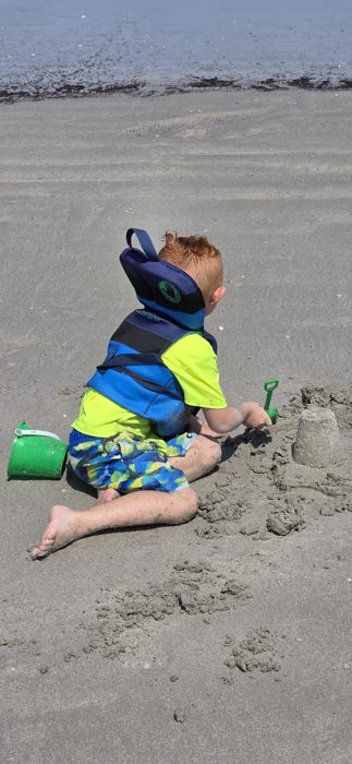 One of the kids builds a sandcastle with the ocean and a crowd of fellow beachgoers stretched out behind him.