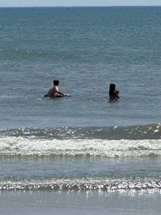 One of the kids paddles out with a parent, both bobbing beyond the breakers with the boogie board in tow.