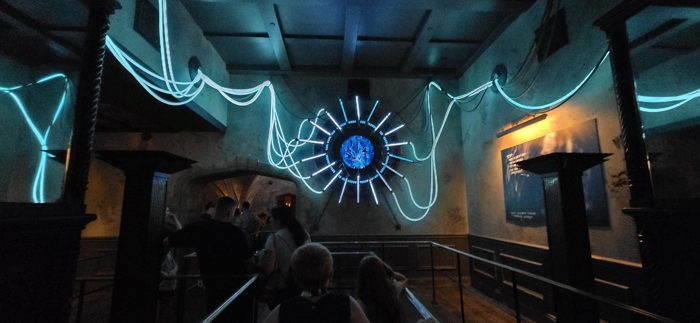 The family winding through a glowing web-lit queue before the ride.