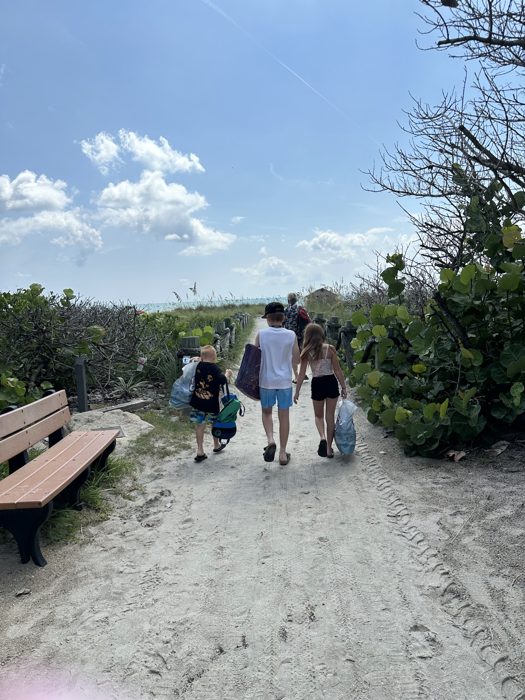 The family treks back up the dune path, towels and gear in hand after a morning at the beach.