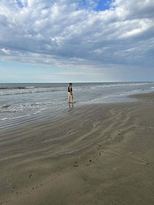 A lone figure out on the wide flat sand under a soft cloudy beach sky.