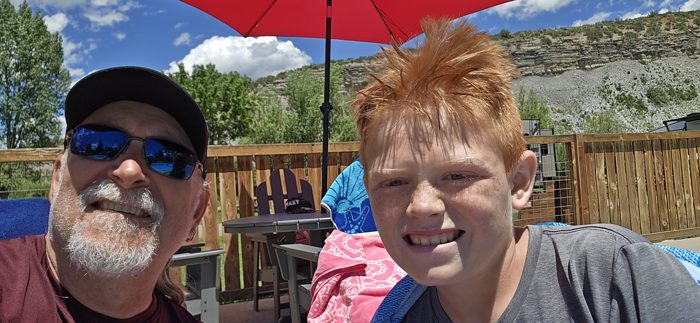 Dad and the redhead lean in close for a sunny poolside selfie under bright blue skies.