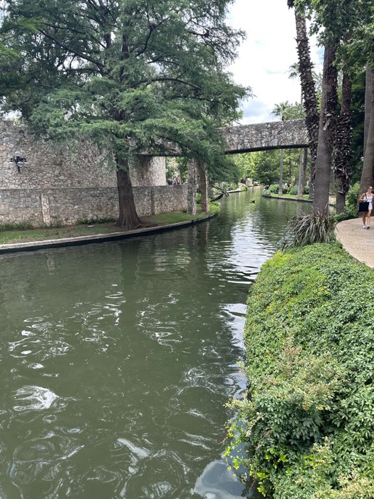 A serene stretch of the River Walk canal slipping under an old stone bridge.