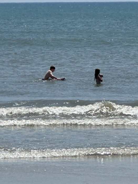 The same two ride out the swells a little further from shore, boogie board floating alongside.