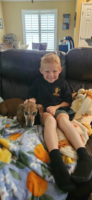 One of the kids relaxes on the couch, giving the old dachshund some pets.