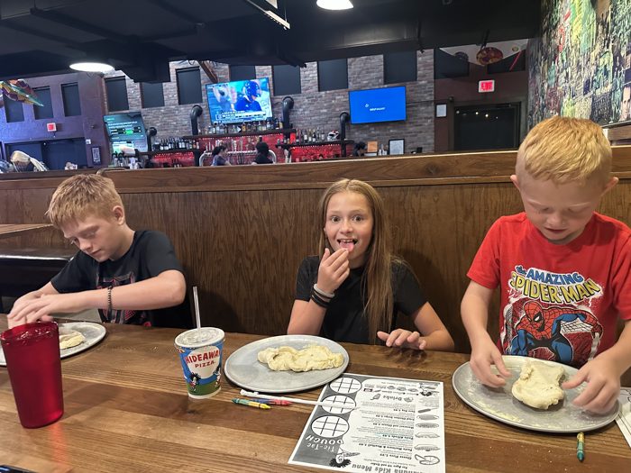 The kids knead their own pizza dough at dinner, one of them sneaking a taste along the way.