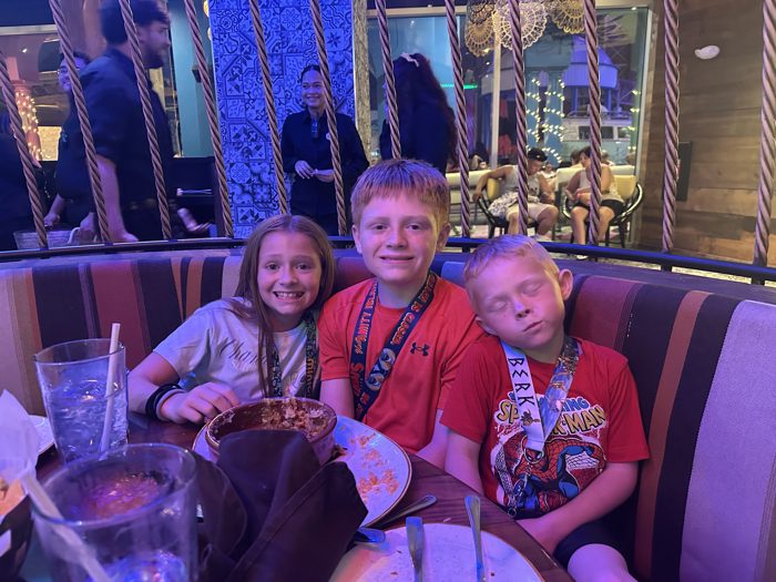 The kids pile into a restaurant booth after a long park day, one of them already dozing off mid-meal.