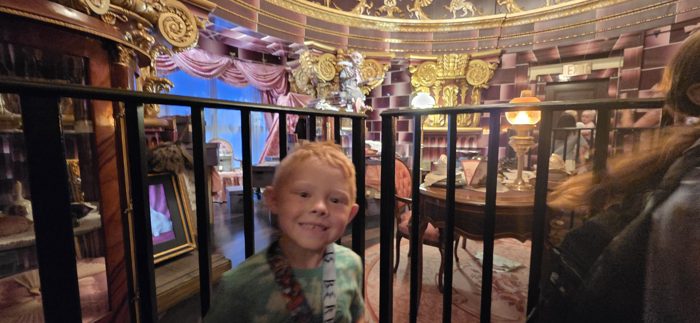 One of the kids grins through the iron rail overlooking an ornate Victorian parlor exhibit.