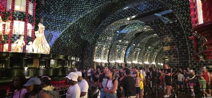A packed queue winds beneath the arched, gold-lit ceilings of the wizarding bank ride.
