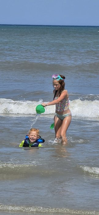 One of the kids pours a bucket of seawater over a giggling sibling bobbing along in a life vest.