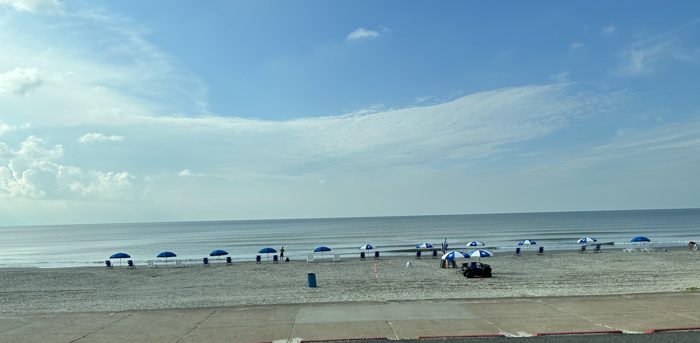 A wide stretch of Gulf-coast beach with cars and beachgoers under a big blue sky.