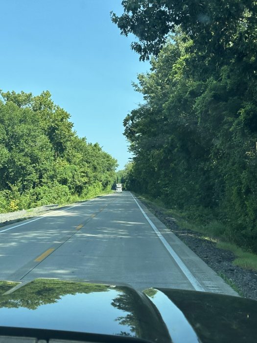 Trailing a truck down a shaded two-lane road, trees arching overhead.