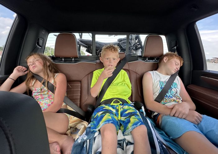 Three worn-out kids slump in the backseat, sunburned and content after a day in the water.