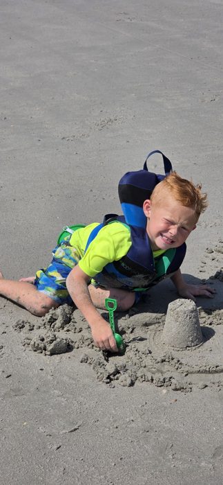 Scrunched-up concentration as one of the kids pats together a small sandcastle on the beach.