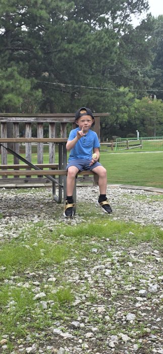 One of the kids strikes a pose on the picnic table bench, snack in hand at the campground playground.