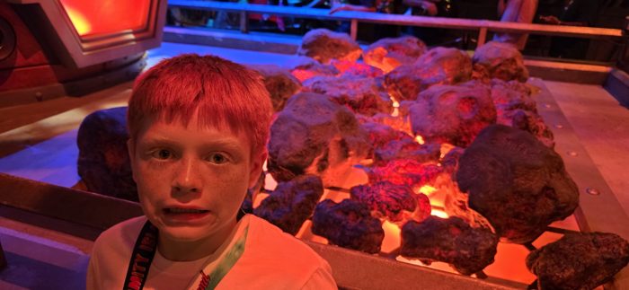 One of the kids wide-eyed next to the glowing lava rocks on the ride set.