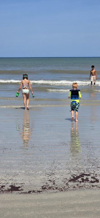 The kids leave rippling reflections in the wet sand as they head back down toward the water.