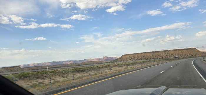 Rolling down the open desert highway, mesas and big sky framed through the windshield.