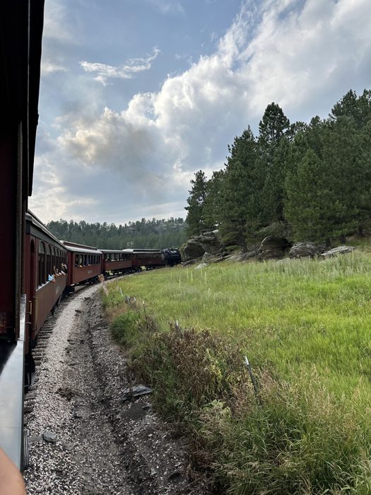 The steam locomotive curving away ahead, white plume rising against a big blue Dakota sky.