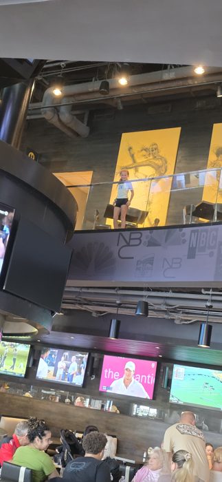 One of the kids strikes a pose on the elevated deck of the sports bar, rows of game-day screens glowing below.