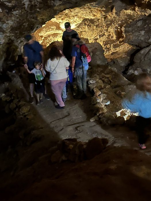 The tour group threads single-file through a warmly lit cave passage.