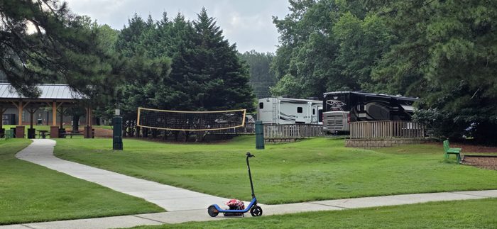 The scooter parked on the path with the volleyball net and rows of rigs spread out behind it.