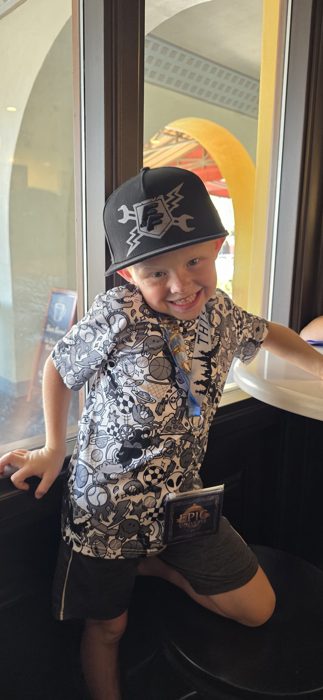 One of the kids grinning in a new ballcap, Epic Universe badge swinging from the lanyard.