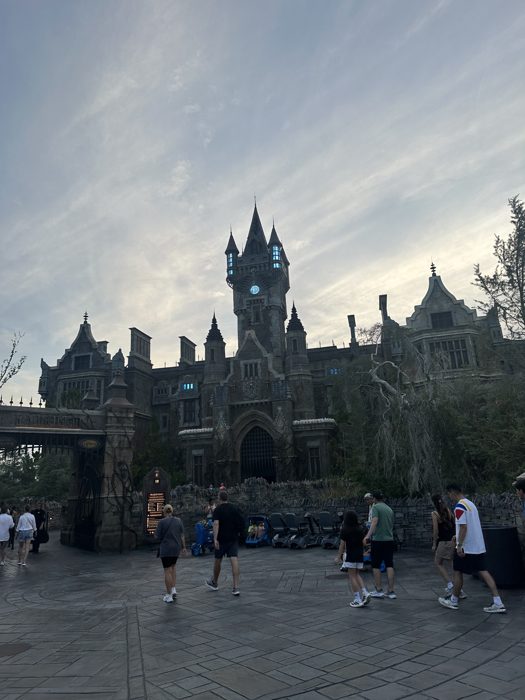 Crowds gather in front of the towering castle as evening settles over the park.