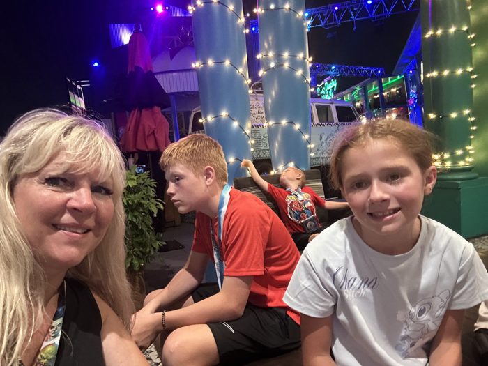 The family gathers for a photo under the glow of colorful lights and neon on a lively evening out.