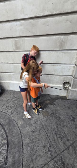 The kids team up on a wand trick, wide-eyed waiting for the magic to work.