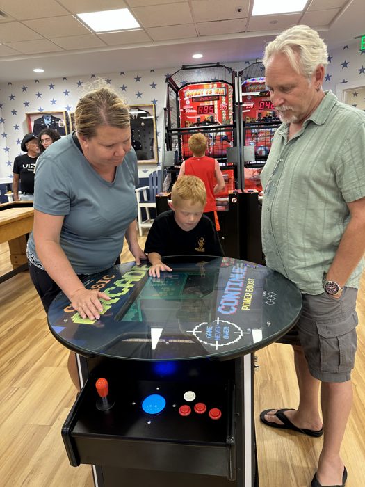 The family crowds around the arcade table as one of the kids takes a turn at classic Pac-Man.