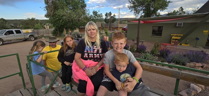 The whole crew piled together on a bench in the sunshine at the dinosaur park.
