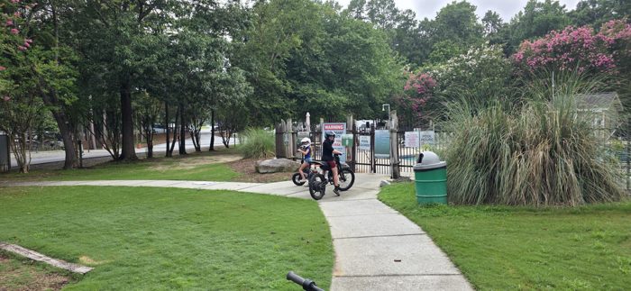 Two of the kids pause on their e-bikes at the pool gate, helmets buckled and ready to ride.