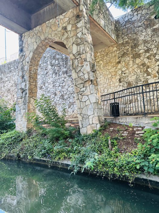 A graceful stone arch bridge crossing the River Walk channel.