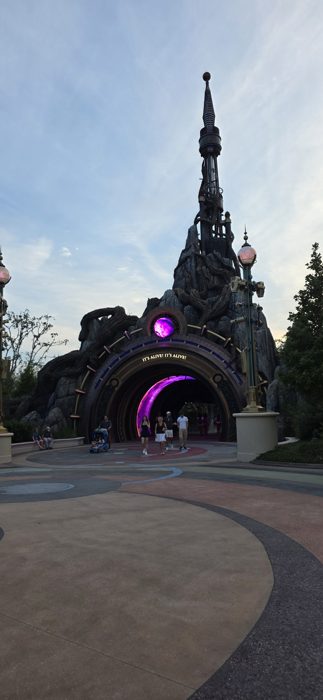 A wider look at the same twilight archway, its neon-lit tunnel pulling everyone in for one more ride.