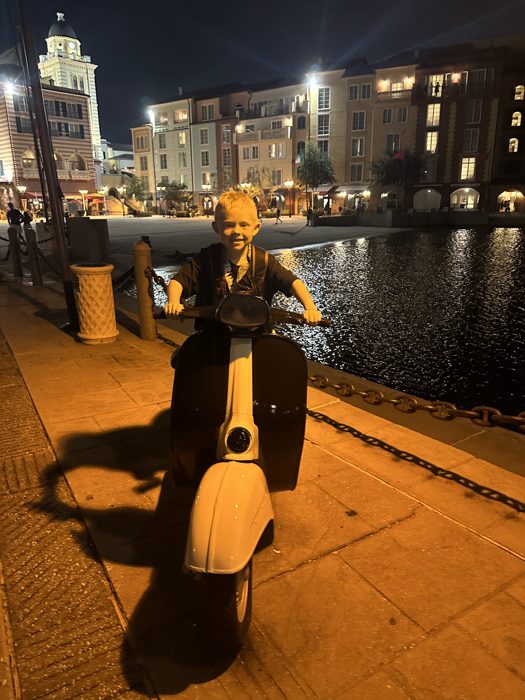 One of the kids poses on a toy scooter along the glowing nighttime harbor walk.
